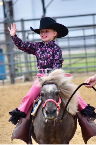 little girl riding a horse waving
